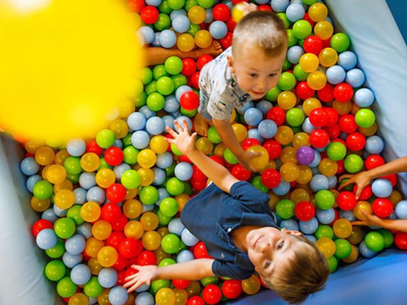 Niños jugando en una piscina de bolas con pelotas de colores en un área de juegos interior.