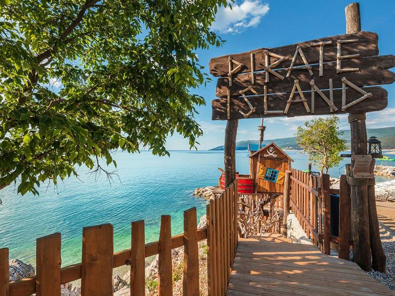 Cartel de madera con la inscripción 'Pirate Island' en la entrada a una zona temática junto al agua.