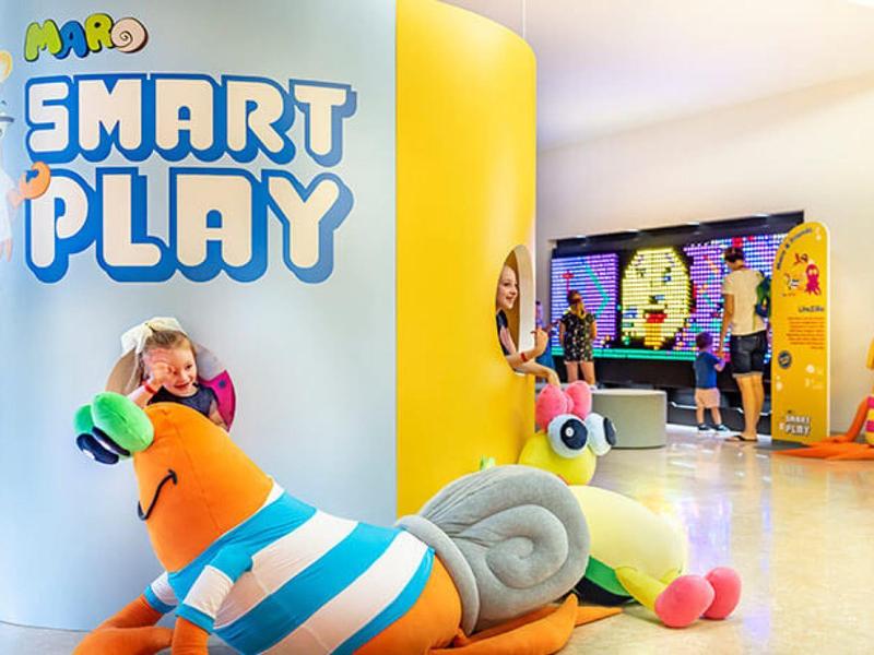 Área de juegos colorida con diferentes figuras y niños en un hotel o centro de ocio.