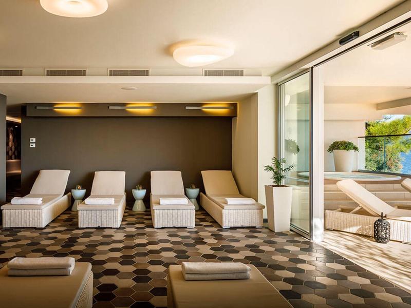 Sala moderna de hotel con tumbonas y grandes ventanales hacia la piscina, luminosa y acogedora.