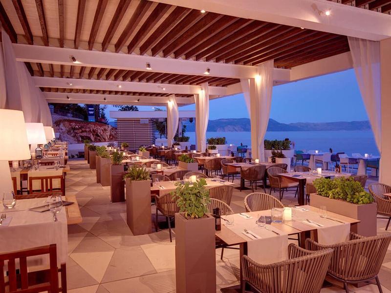 Restaurante abierto con techo de madera y vista al mar al atardecer.
