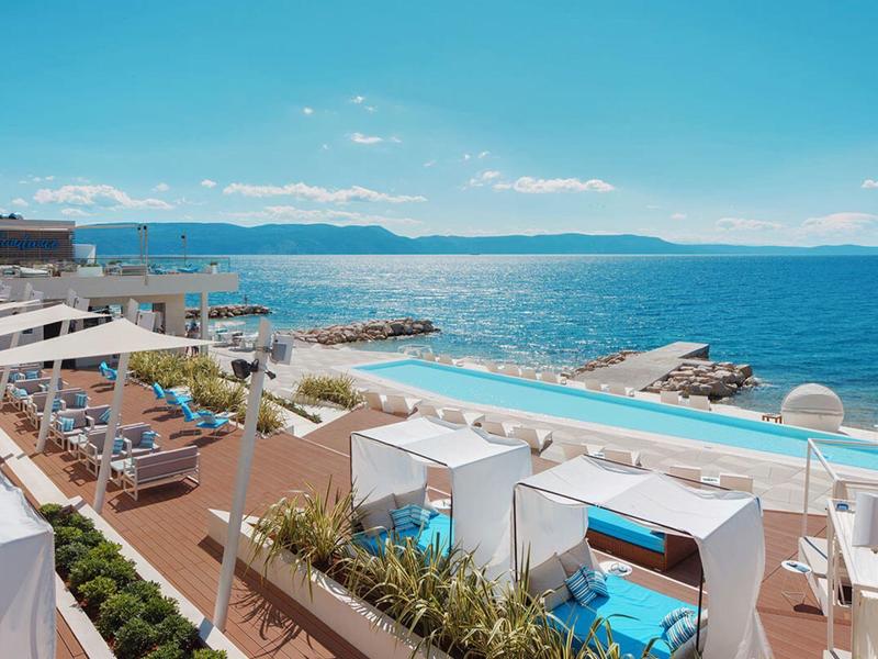 Piscina moderna del hotel con tumbonas y vista al mar azul bajo un cielo despejado.