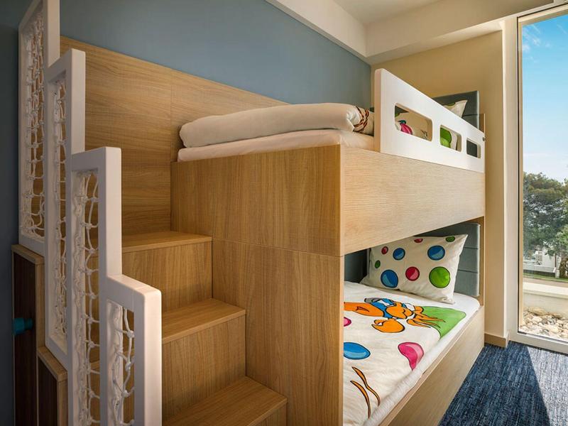 Litera moderna de madera con colchones de colores junto a ventana abierta con vista exterior.