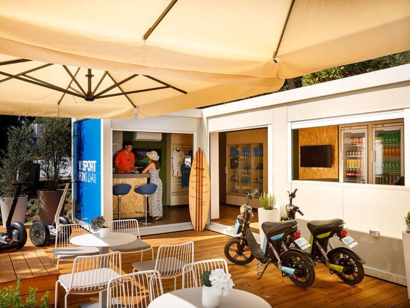 Área exterior moderna de un hotel con asientos y dos motocicletas bajo sombrillas.