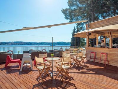 Taras z drewnianą podłogą, krzesłami i stołami z widokiem na jezioro i las