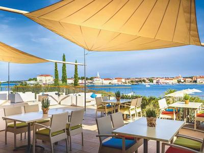 Taras z stołami, krzesłami i markizami z widokiem na morze i miasto w tle