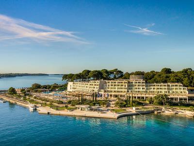 Hotel na wybrzeżu z widokiem na niebieskie morze, otoczony drzewami przy czystym niebie.
