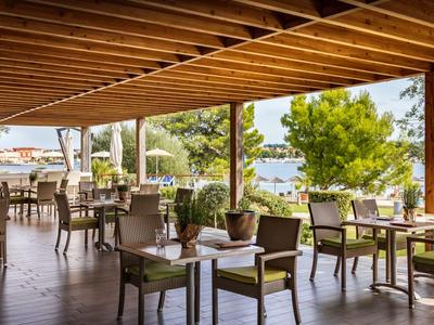 Zadaszony taras z stolikami i widokiem na morze i miasto w tle.