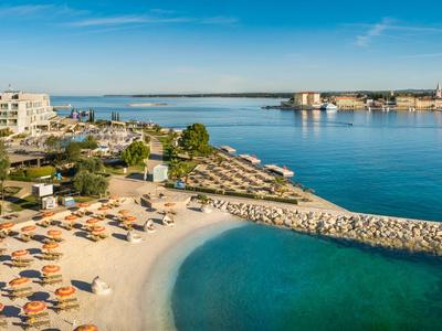 Strand mit vielen Sonnenschirmen, blaues Meer und moderner Küstenbebauung im Hintergrund.