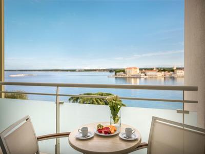 Balkon met tafel, stoelen, ontbijt en uitzicht op rustige zee bij heldere lucht.