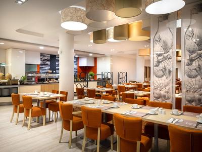 Nowoczesna restauracja z jasnymi ścianami, pomarańczowymi krzesłami i dekoracyjnymi panelami ściennymi.