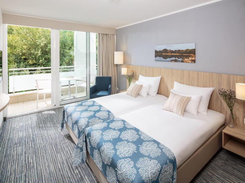 Modern hotelkamer met twee eenpersoonsbedden, balkon en uitzicht op groen.