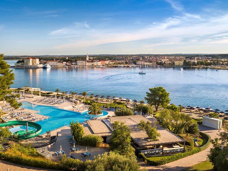Uitzicht op een hotel met zwembad en glijbaan aan de oever van een kalm meer bij helder weer.