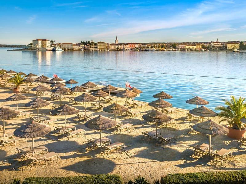 Zonnig zandstrand met ligstoelen en uitzicht op kalm water en verre stad.