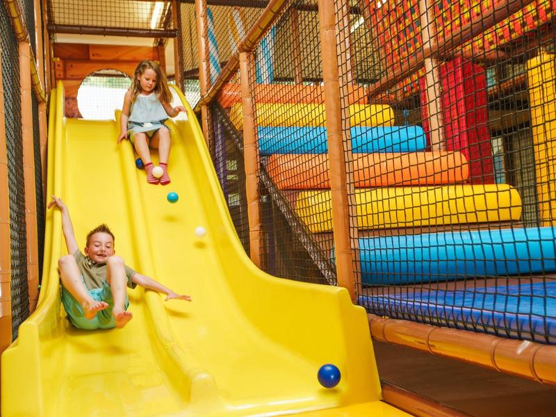 Vader en dochter glijden samen van een gele glijbaan in een binnen speelzone.