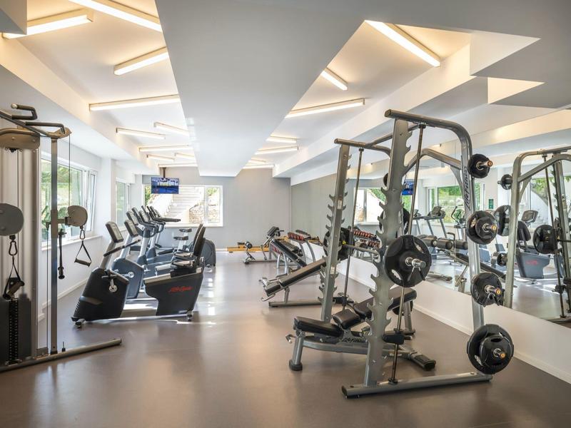 Lichte fitnessruimte met moderne apparatuur en grote ramen die natuurlijk licht binnenlaten.