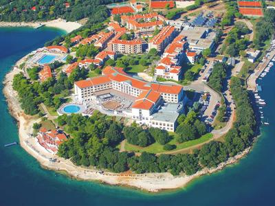 Aerial view of a waterfront hotel with red roofs and surrounding trees on a peninsula.