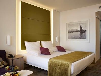 Modern hotel room with large bed, lighting, and decorative wall picture.