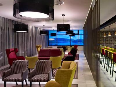 Salon moderne d'hôtel avec fauteuils colorés et sièges, éclairé par des lampes au plafond.