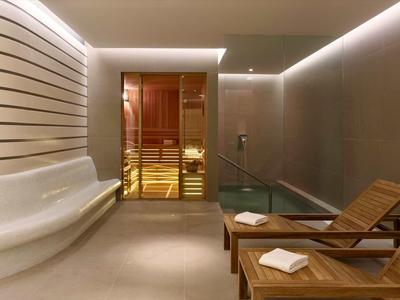 Modern relaxation room with lounge chairs, water feature, and sauna in background.