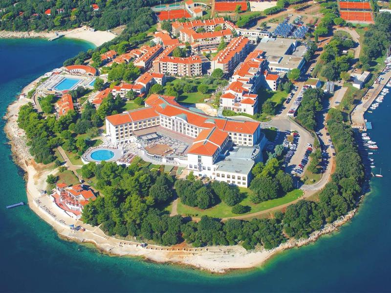 Aerial view of a waterfront hotel with red roofs and surrounding trees on a peninsula.