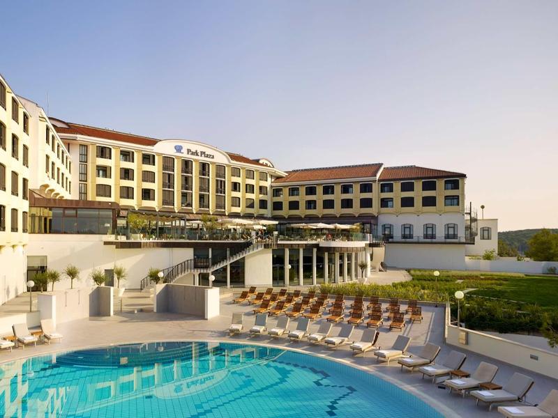 Large hotel with outdoor pool and sun terrace under clear sky.