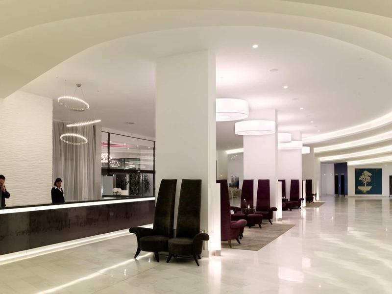Modern hotel lobby with curved ceiling, reception desk, and seating areas.