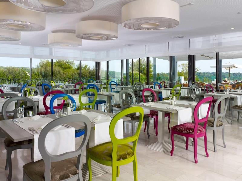 Spacious dining area with colorful chairs and large windows overlooking green landscape.