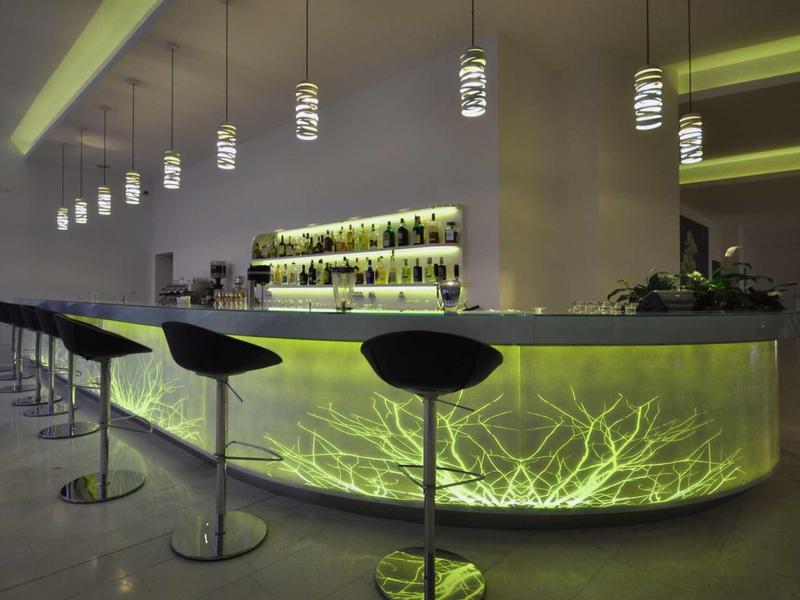 Modern hotel bar with backlit, green illuminated counter and black bar stools.