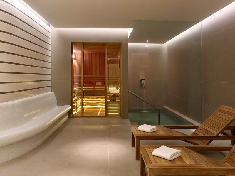 Modern relaxation room with lounge chairs, water feature, and sauna in background.