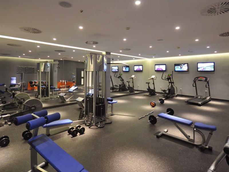 Well-lit gym with various exercise machines and weight benches.