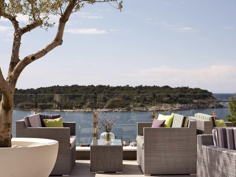 Terrace with modern seating and a view of the sea and a wooded bay.