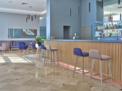 Zone de bar d'hôtel moderne avec tabourets, accents en bois et sièges confortables en arrière-plan.