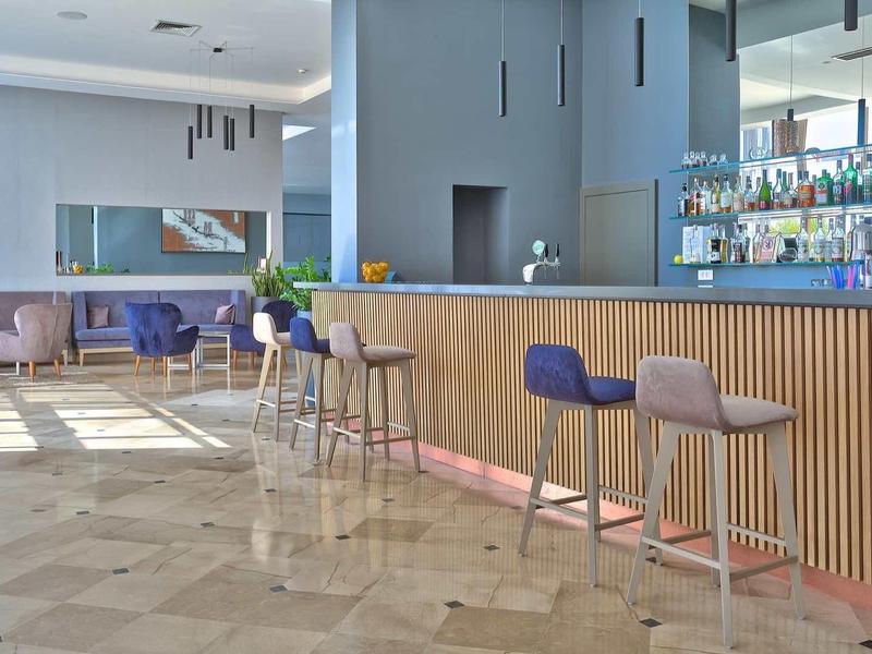 Moderní hotelový bar s dřevěným pultem, barovými stoličkami a pohodlným lounge v pozadí.