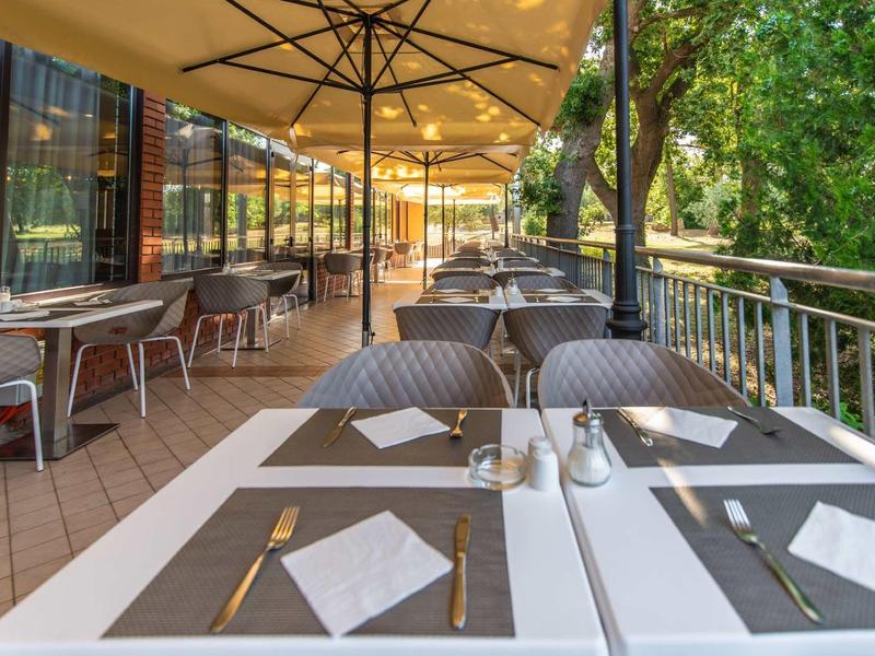 Terasa restaurace s prostřenými stoly a slunečníky vedle řeky.