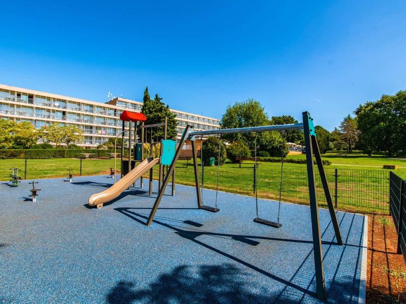 Dětské hřiště se skluzavkami a houpačkami před budovou hotelu pod jasnou oblohou.