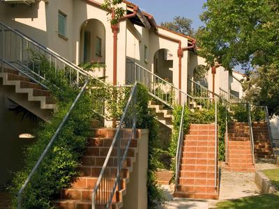 Fila di case a schiera su due piani con scale e ringhiere metalliche sotto alberi verdi.