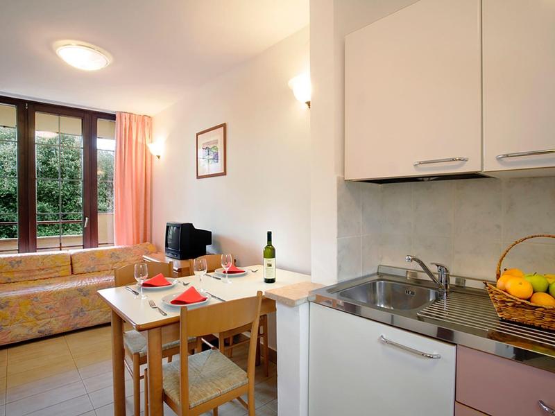 Útulný rekreační byt s malou kuchyní, jídelním stolem a posezením u velkého okna.