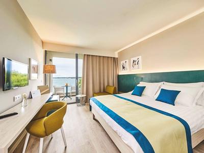 Habitación de hotel moderna con cama grande, escritorio, TV y balcón con vista al mar.