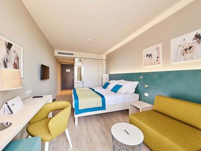 Habitación de hotel moderna con cama doble, sofá verde y área de escritorio.