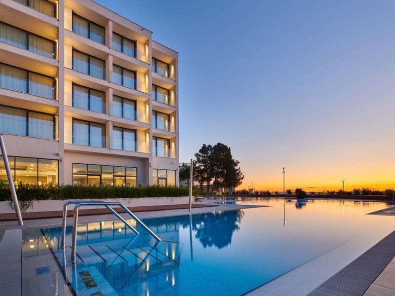 Moderner Pool neben Gebäude mit Glasfenstern, Sonnenuntergang und klarer Himmel im Hintergrund.