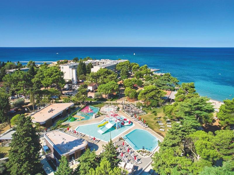 Blick auf ein Hotelresort mit mehreren Pools, umgeben von Bäumen und Meer im Hintergrund.
