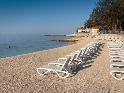 Chaises longues vides sur la plage de galets avec vue sur la mer calme sous un ciel dégagé.