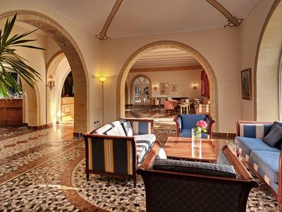 Un salon d'hôtel élégant avec des fauteuils rembourrés et des canapés devant de grandes portes cintrées.