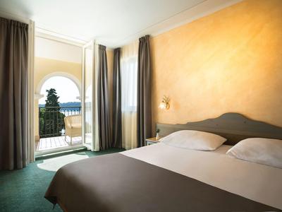 Habitación de hotel luminosa con cama doble, cortinas y balcón con vista al mar.