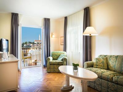 Habitación de hotel luminosa con sofá, sillón, mesa y balcón con vista al mar.