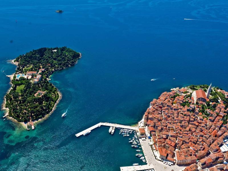 Aerial view of a small, densely built island next to a forested island in blue sea.