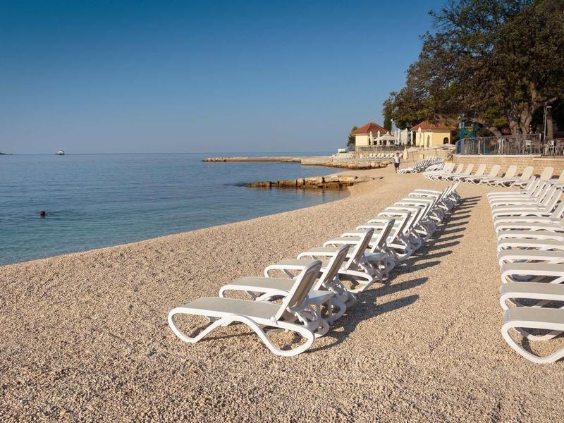 Row of white sun loungers on a quiet beach with clear sky and calm sea.