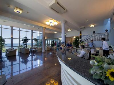 Hotelhal met receptie, zitgedeelte en grote glazen wand met zeezicht