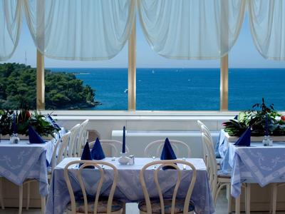 Een elegant restaurant met wit bedekte tafels en uitzicht op de blauwe zee.